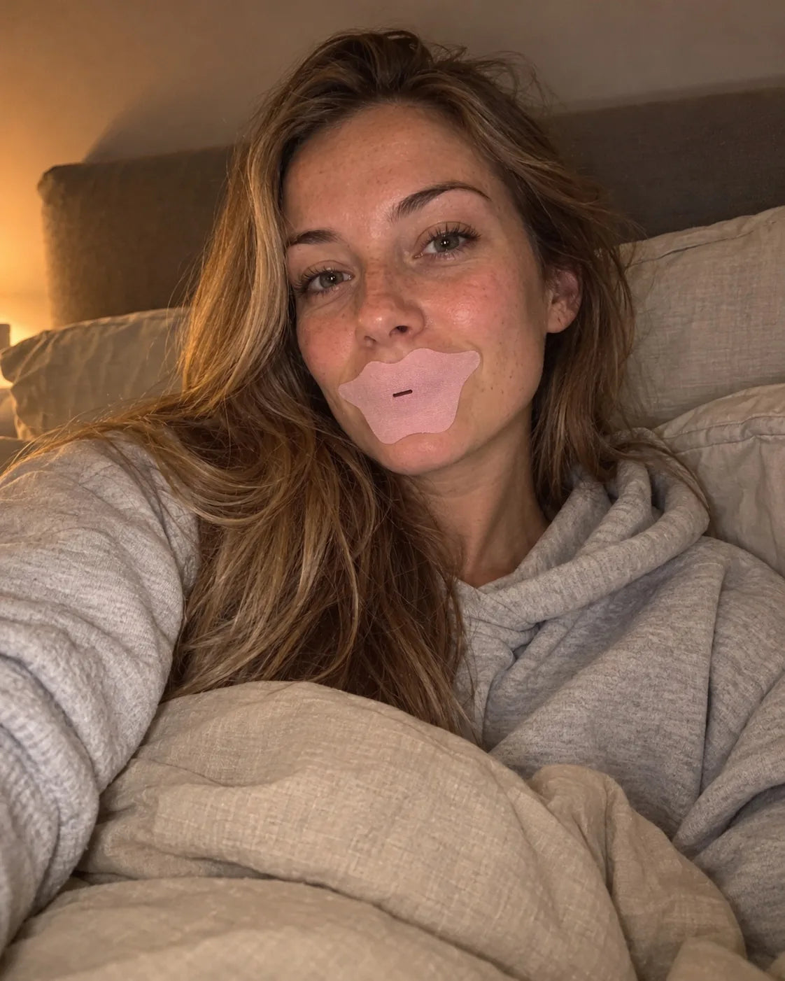 Kvinde i seng med den lyserøde Comformidable kollagenmundtape på, med åbning i midten